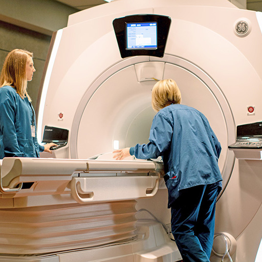 Two MRI technologists work with an MRI scanner.