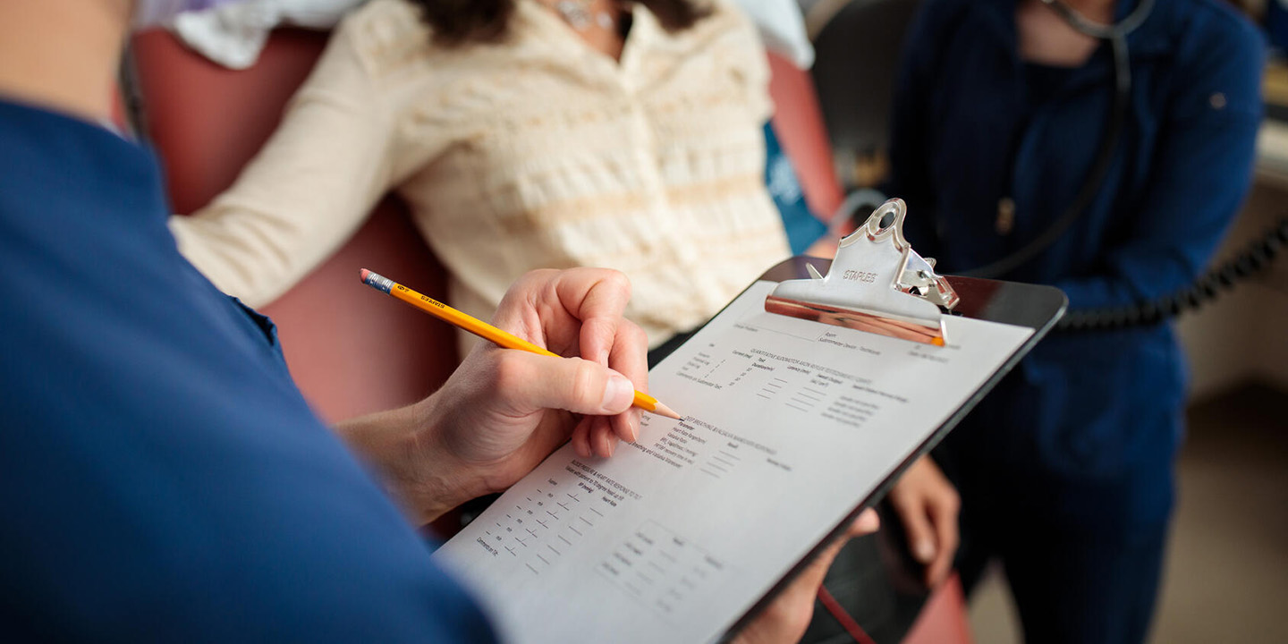 A Clinic Neurophysiology Technologist at Mayo Clinic takes notes on a clipboard while examining a patient